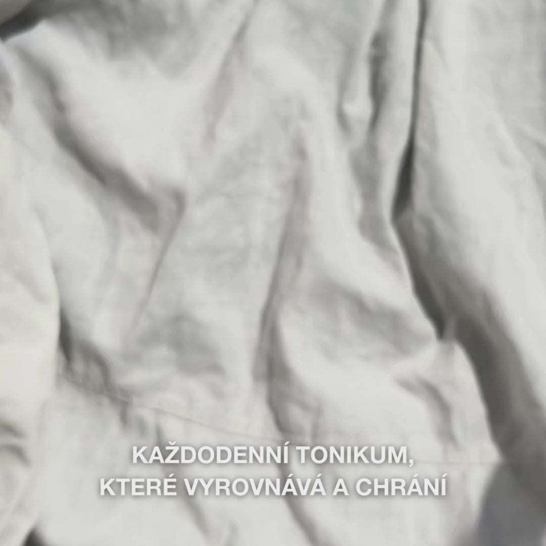 Detail ruky, která jemně nanáší několik kapek čirého tonika Face Tonic s tea tree olejem na vatový tamponek a poté ho jemně stírá po čisté pokožce obličeje: lehká, osvěžující tekutina zklidňuje, hloubkově čistí, hydratuje a zanechává pleť obnovenu a lehce připravenou na následný krém.