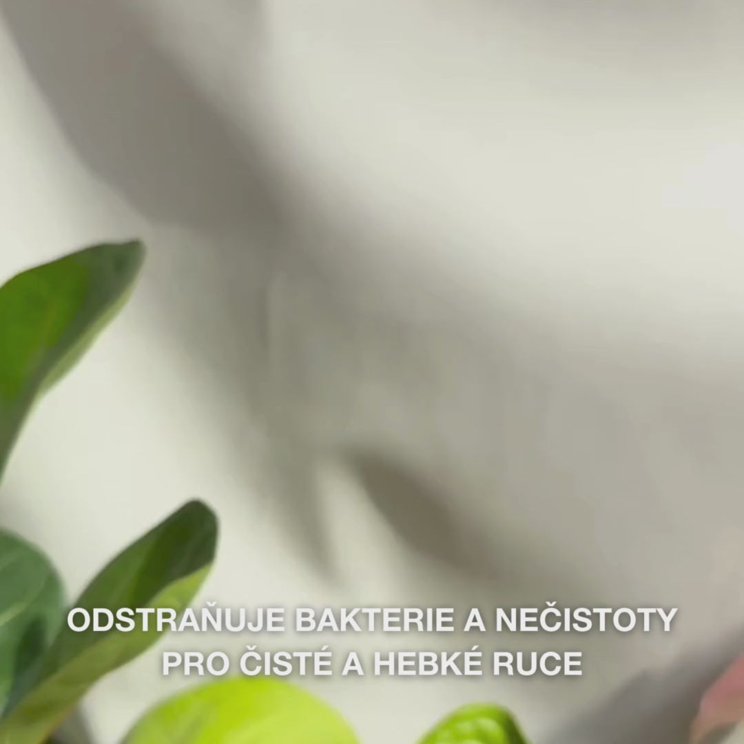 Detail rukou, které dávkují jasně modré, pěnivé tekuté mýdlo s Tea Tree Oil do dlaně, a následně jemně myjí dlaně, hřbety rukou a mezi prsty — textura jemné, čistící pěny odstraňuje bakterie a nečistoty, zatímco změkčuje a zvlhčuje pokožku.