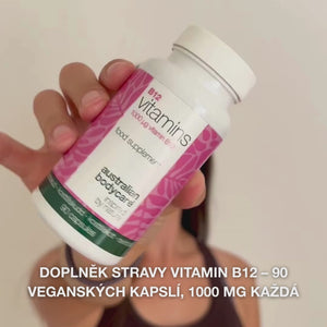 Detail ruky držící lahvičku doplňku stravy Vitamin B12, otevírá víčko a vysypává hladké bílé kapsle – ukázka produktu pro každodenní užívání na podporu energie, imunity, nervového systému a snížení únavy.